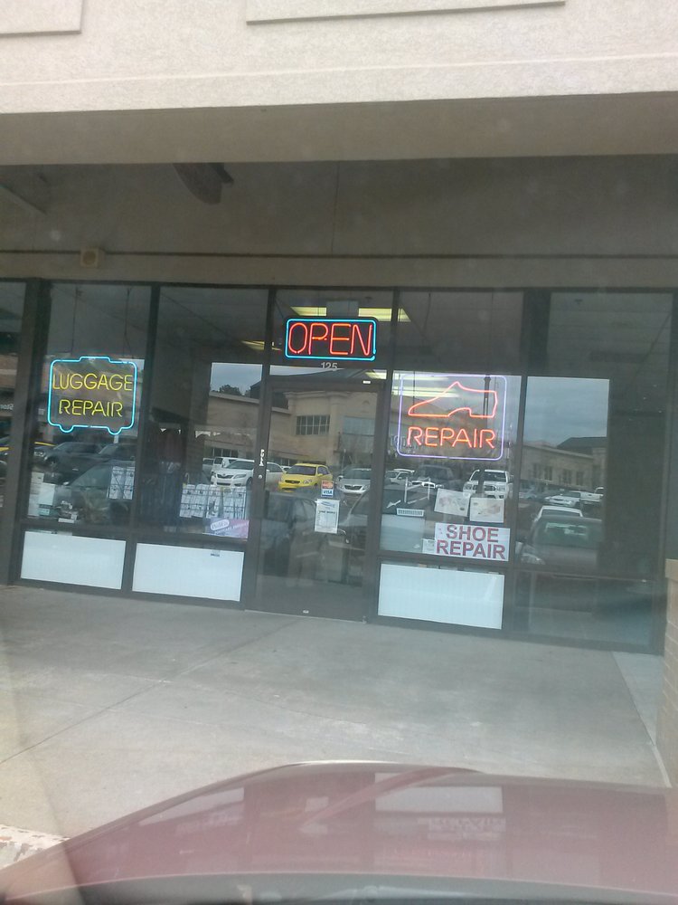 The shop front at suite 125, with a cyan LUGGAGE REPAIR neon sign in the left window, an OPEN sign above the door, and a red neon shoe with the word REPAIR in the right window.